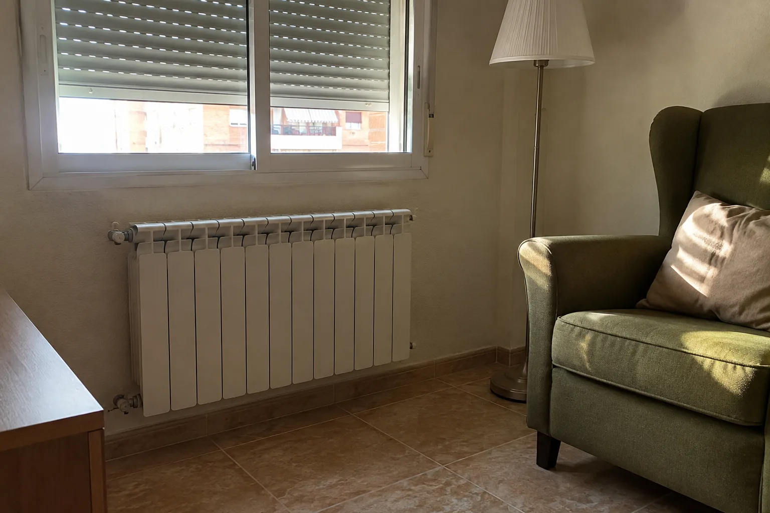 Radiador junto a una ventana con persiana y un sillón de lectura